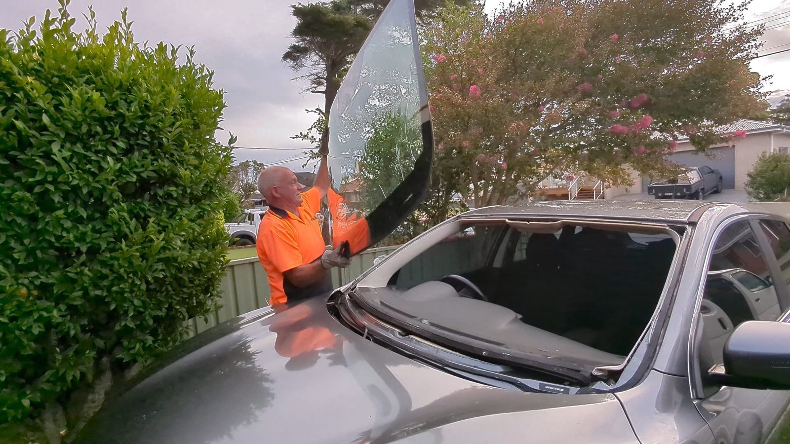 Fitting a new windscreen to a grey sedan in a driveway